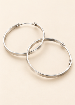 Coppia di orecchini Orbita Libera a cerchio con fascia piatta e chiusura a filo curvo, su fondo crema.