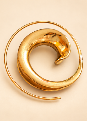 Dettaglio di un orecchino Vortice Solare in ottone: spirale bombata e concava con sottile filo curvo esterno; diametro 3 cm.