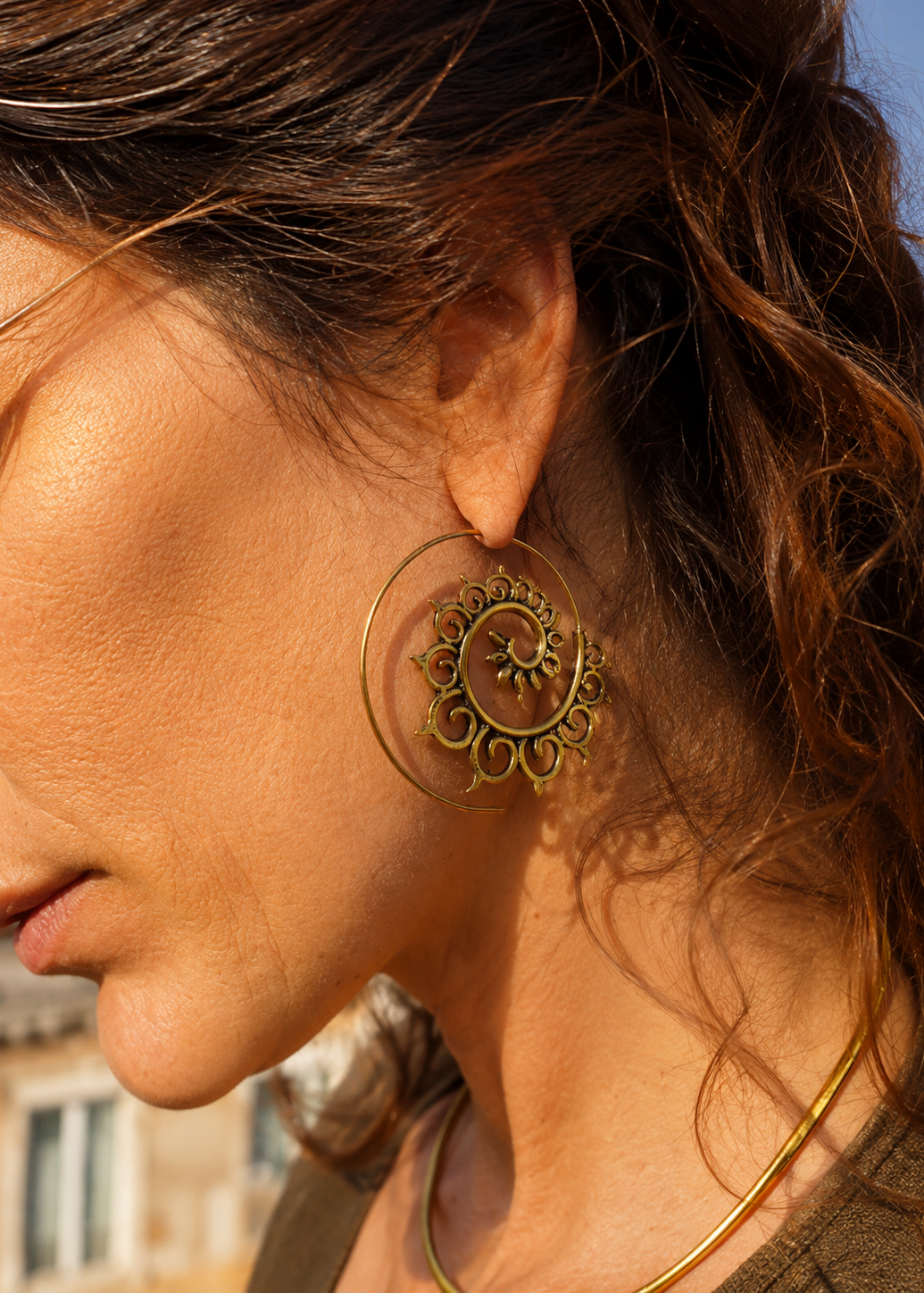 Donna di profilo indossa un grande orecchino a spirale in ottone con motivo mandala