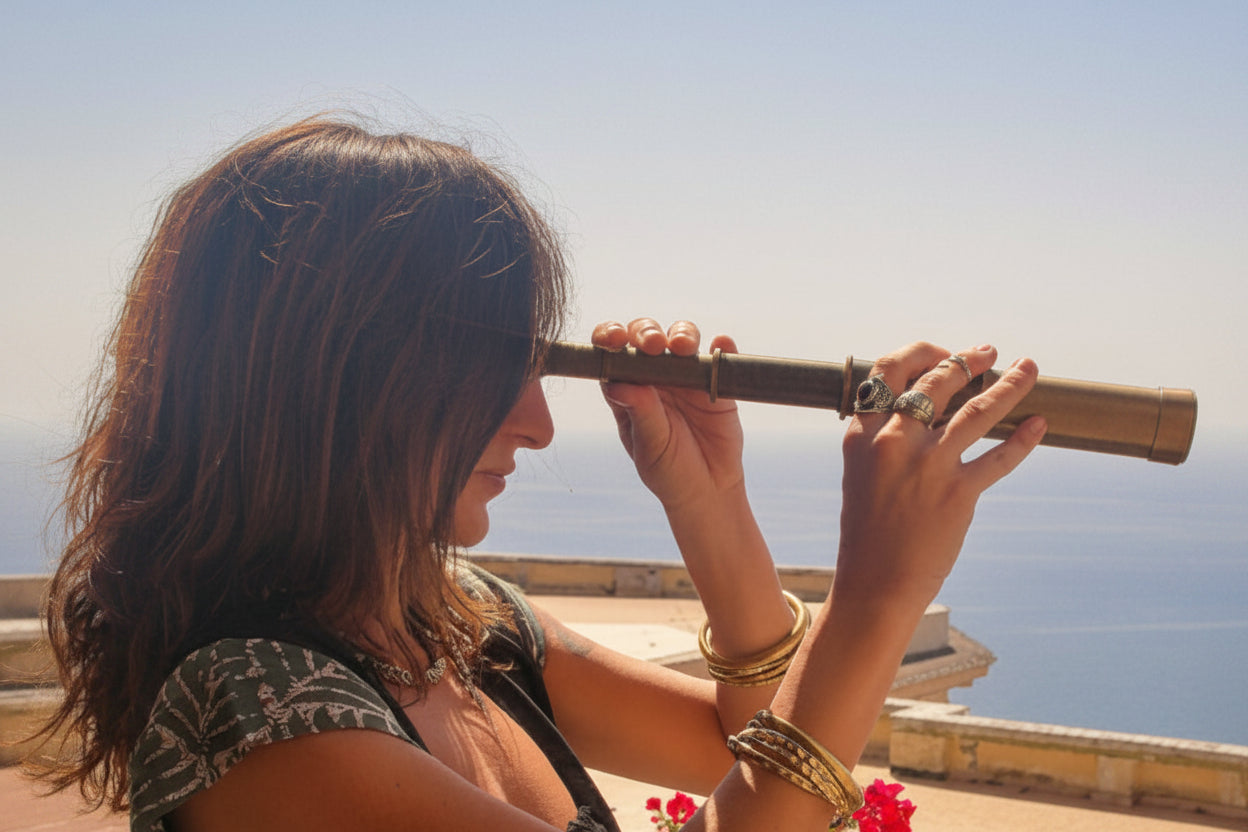 Donna con gioielli boho dorati guarda il mare con cannocchiale